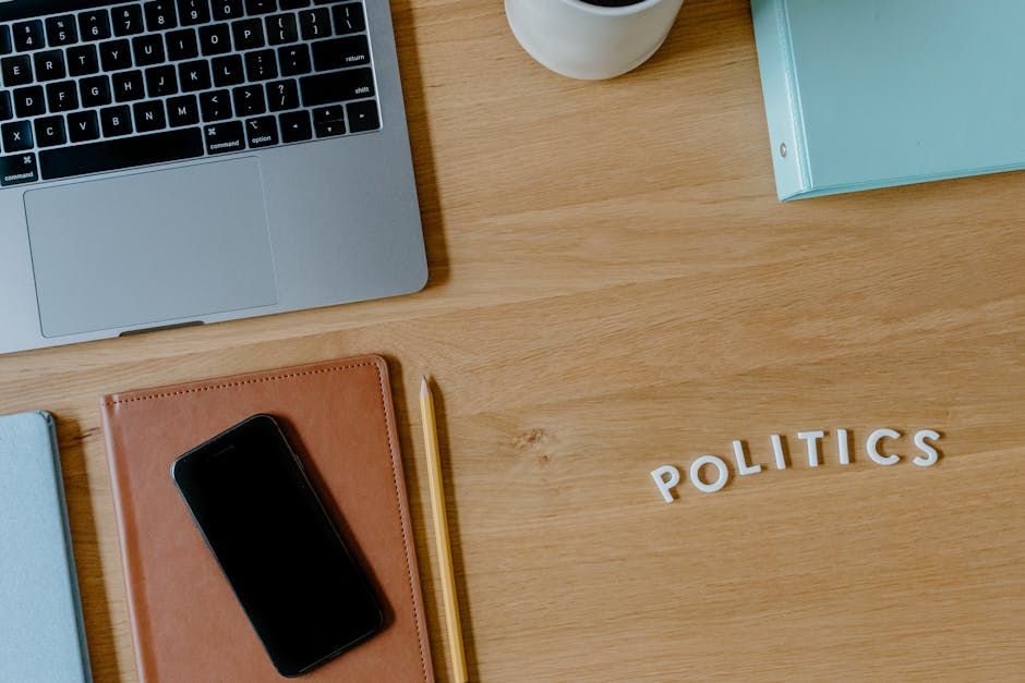 A top view of a workspace featuring a laptop, smartphone, and 'politics' text on a wooden desk.