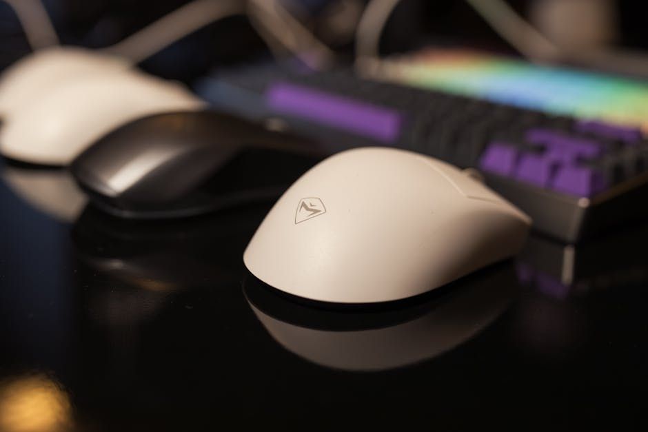 A sleek computer mouse next to a colorful gaming keyboard on a reflective surface.