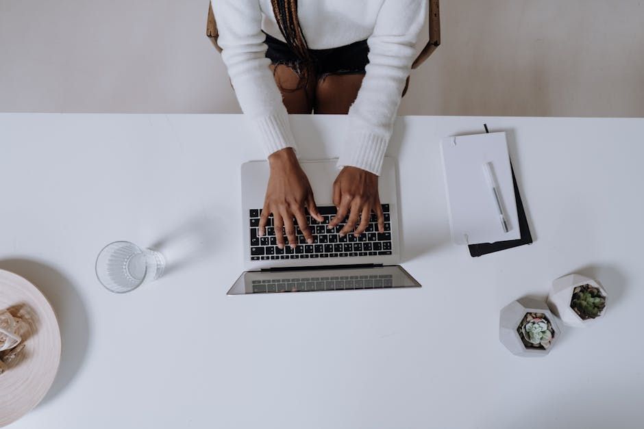 Top view of a woman typing on a laptop at a modern, minimalist home office desk with plants.
