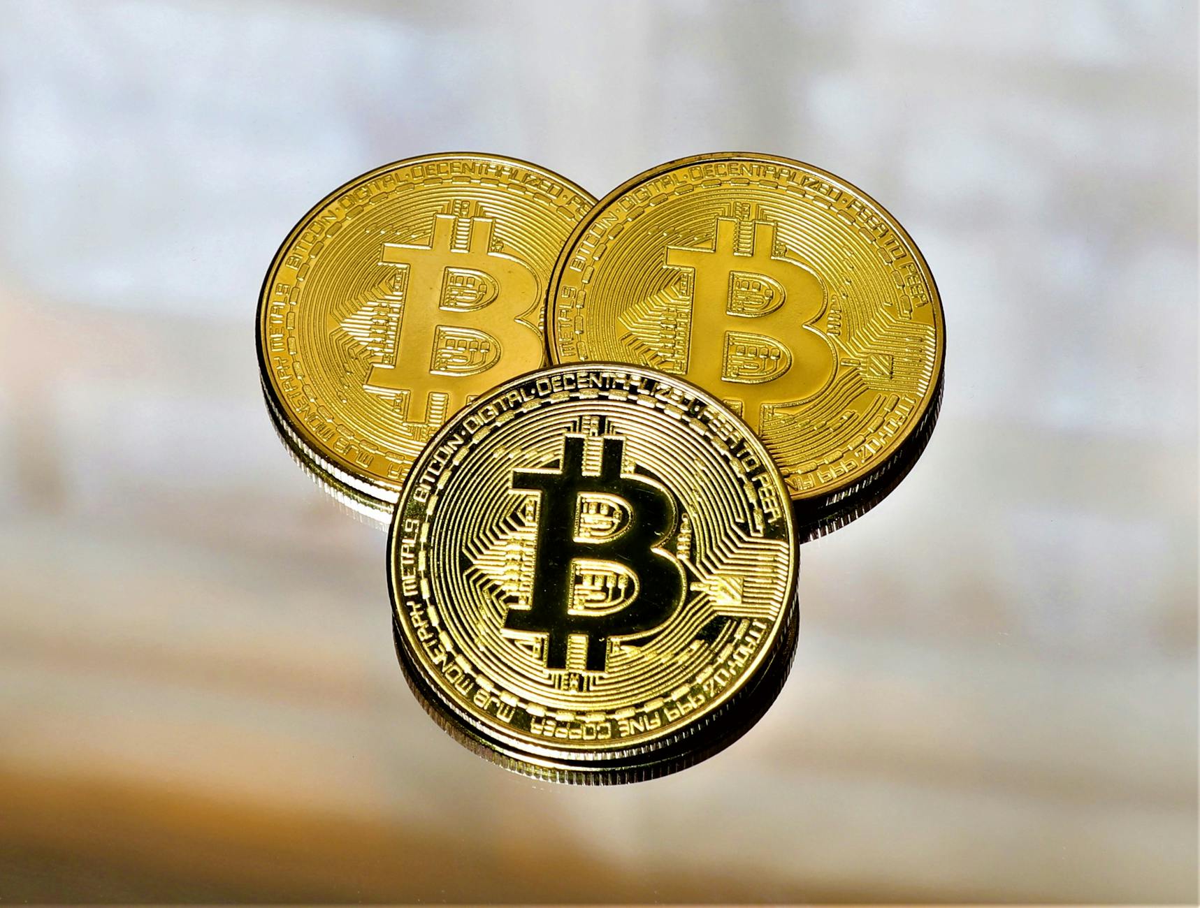 Close-up of three gold Bitcoin coins on a reflective surface highlighting cryptocurrency and finance.