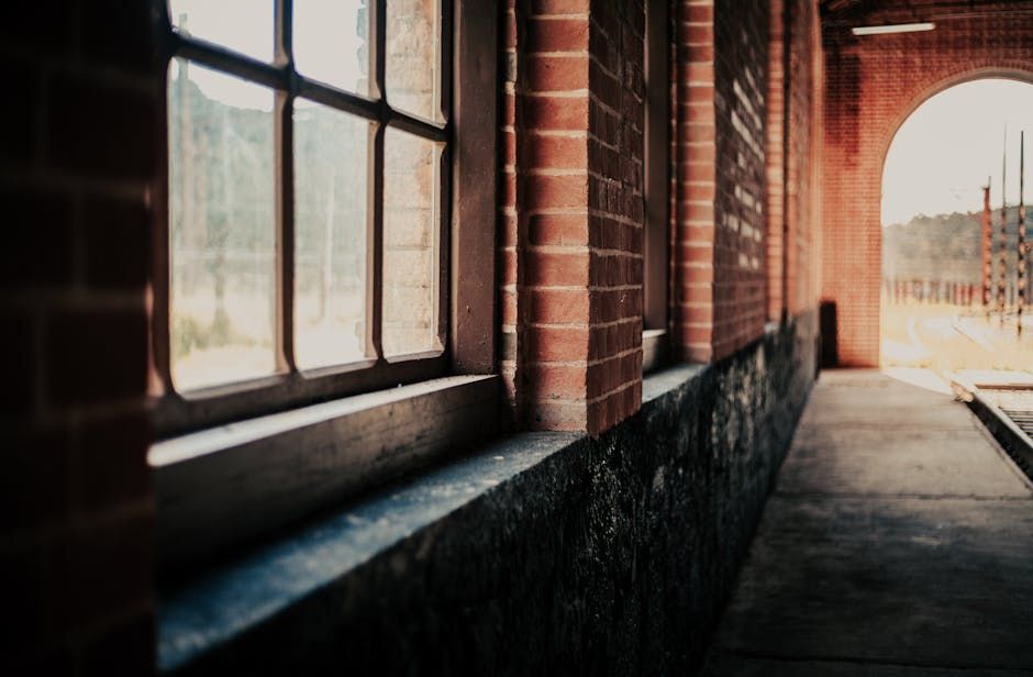A rustic corridor in a historic train station with brick walls and large windows.
